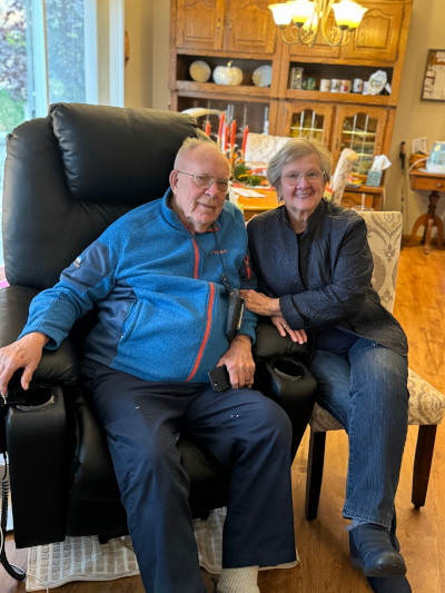 Smiling client from Visiting Angels of Spokane, wearing blue shirt, seated in a chair, and wearing glasses.